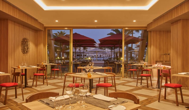 Himitsu Interior of a modern Japanese restaurant featuring warm wood-paneled walls, minimalist wooden tables with red cushioned chairs at Dreams Lanzarote Playa Dorada Resort & Spa by Kenwood Travel