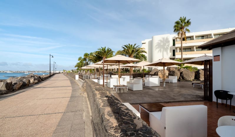 Sugar Reef modern seating and beige umbrellas overlooking the ocean boardwalk at Dreams Lanzarote Playa Dorada Resort & Spa by Kenwood Travel