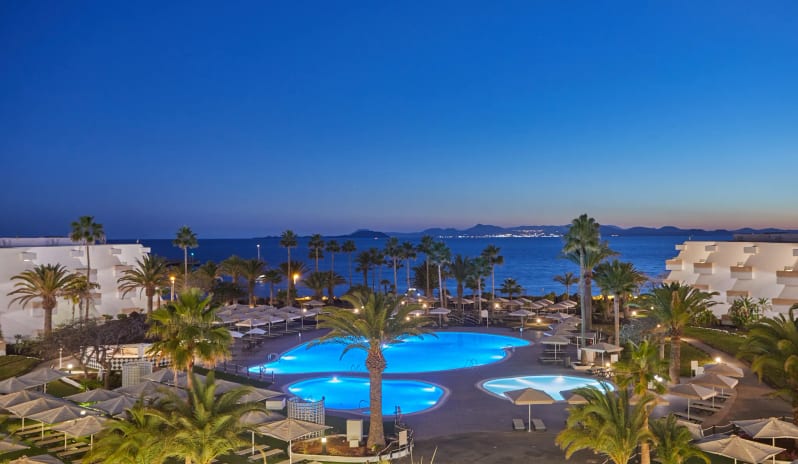 Barracuda swimming pools at a luxury seaside resort in Lanzarote, featuring palm trees and a view of the ocean horizon at Dreams Lanzarote Playa Dorada Resort & Spa by Kenwood Travel