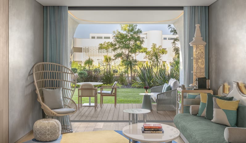 Superior Two Bedroom Suite featuring a light gray sectional sofa, blue textured rug, and large sliding doors opening to a private garden terrace with lounge seating at W Algarve by Kenwood Travel