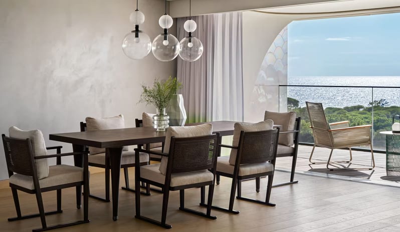 Supreme Three-Bedroom Residence Minimalist luxury dining interior with large sliding glass doors leading to a scenic balcony, featuring neutral grey walls and contemporary lighting at W Algarve by Kenwood Travel