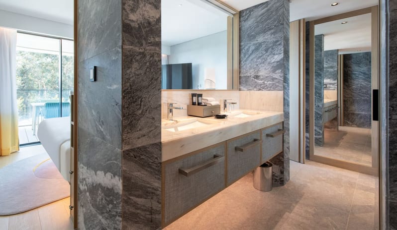 Supreme Three-Bedroom Residence Luxury bathroom interior with contemporary dual sinks, large vanity mirror, and natural stone finishes in a bright, open-concept hotel suite at W Algarve by Kenwood Travel