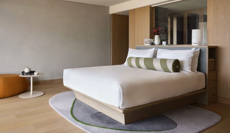 Supreme Three-Bedroom Residence master bedroom featuring a platform bed with crisp white linens, a sage green striped bolster pillow, and light wood paneled walls at W Algarve by Kenwood Travel