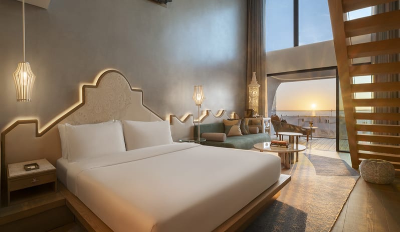 W Suite with Plunge Pool, One Bedroom Suite bedroom suite at a luxury resort featuring minimalist wood furniture, warm ambient lighting, and floor-to-ceiling windows with a sunset sea view at W Algarve by Kenwood Travel