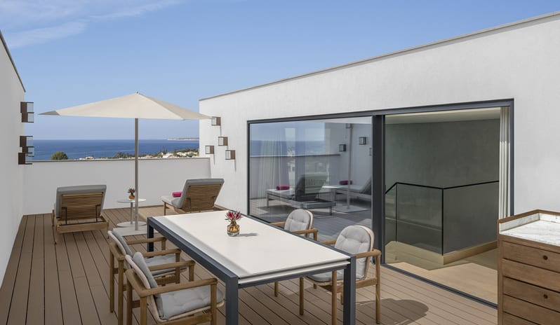 W Suite with Plunge Pool, One Bedroom Suite rooftop terrace of a luxury suite featuring a modern outdoor dining set, lounge chairs under a cream umbrella, and panoramic views of the ocean coast at W Algarve by Kenwood Travel