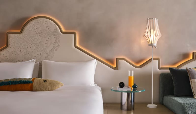 Premier Deluxe Room featuring a cream headboard with an intricate mandala pattern and warm integrated LED backlighting, accompanied by a modern floor lamp and a glass-top side table at W Algarve by Kenwood Travel