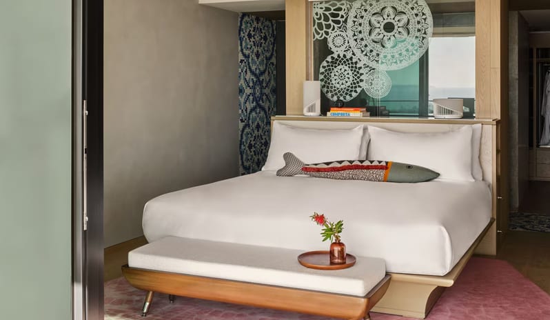 Penthouse I, Two Bedroom Suite with Pool bedroom featuring a white plush bed with a decorative fish-shaped pillow, a wooden end-of-bed bench, and blue Portuguese-style tile accents at W Algarve by Kenwood Travel