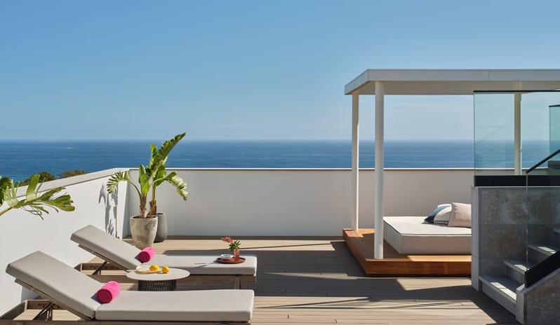 Penthouse I, Two Bedroom Suite with Pool rooftop terrace overlooking the ocean, featuring two modern grey sun loungers with pink towels, a wooden platform with a white cabana daybed, and tropical potted plants at W Algarve by Kenwood Travel