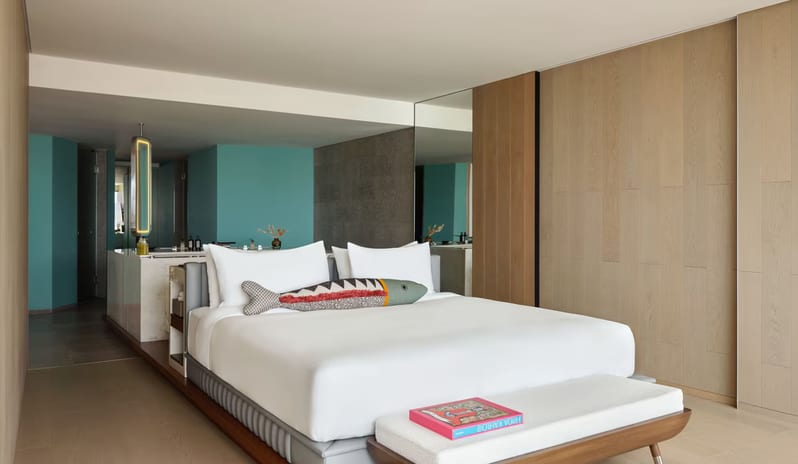 Penthouse II Suite, One Bedroom Suite with Pool featuring a white bed with a decorative fish pillow, light wood wall paneling, and an open-concept bathroom with teal accents at W Algarve by Kenwood Travel