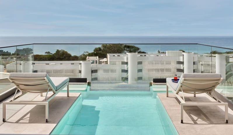 Penthouse II Suite, One Bedroom Suite with Pool rooftop terrace featuring a narrow infinity-edge plunge pool flanked by two modern sun loungers, overlooking a coastal resort and the ocean under a clear sky at W Algarve by Kenwood Travel
