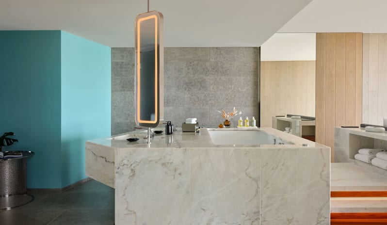 Penthouse II Suite, One Bedroom Suite with Pool bathroom featuring a large white marble island with an integrated bathtub and sink, a vertical glowing LED mirror, and a vibrant teal accent wall at W Algarve by Kenwood Travel