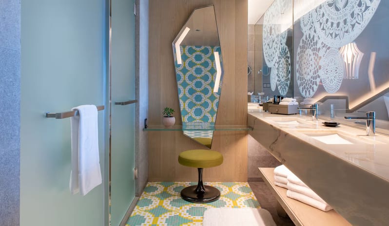 Premier Private Garden Room bathroom design with a floating marble sink, glass shelving, a decorative mandala-patterned wall, and frosted glass shower doors at W Algarve by Kenwood Travel