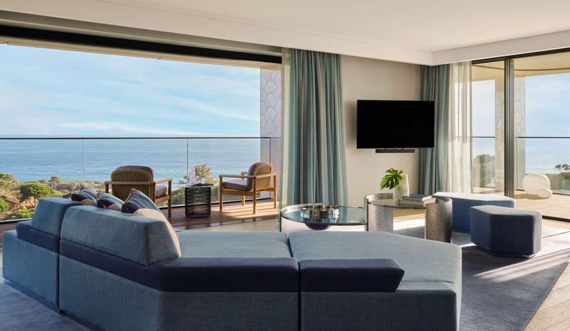 Penthouse I, Two Bedroom Suite with Pool living area with a large blue modular sectional sofa, floor-to-ceiling windows opening to a private terrace with ocean views, and two contemporary armchairs at W Algarve by Kenwood Travel