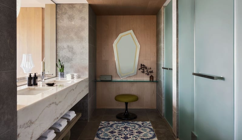 Premier Two-Bedroom Residence bathroom at W Algarve featuring a double marble vanity, a geometric backlit mirror over a glass makeup desk, and Portuguese-style blue tile flooring accents at W Algarve by Kenwood Travel