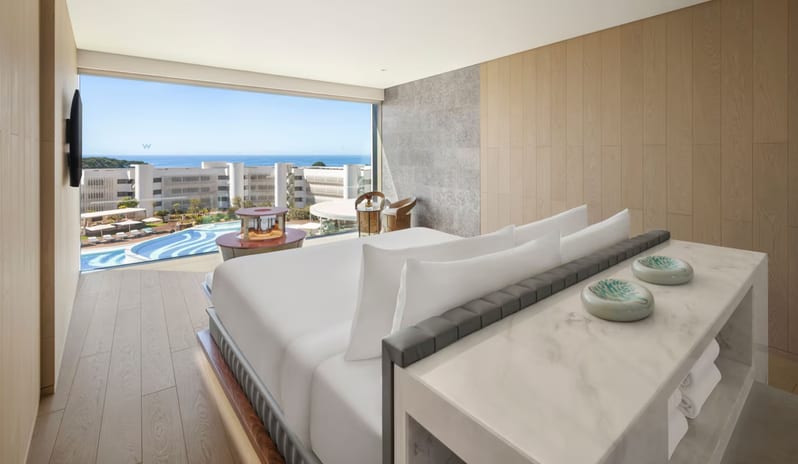 Penthouse II Suite, One Bedroom Suite with Pool bedroom with floor-to-ceiling windows overlooking a resort pool and the ocean, featuring light wood floors and a white marble vanity at W Algarve by Kenwood Travel