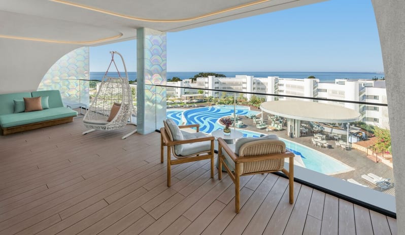Penthouse II Suite, One Bedroom Suite with Pool terrace with wood-plank flooring, featuring a white hanging egg chair, a teal daybed, and wooden armchairs overlooking a wavy resort pool and the ocean at W Algarve by Kenwood Travel