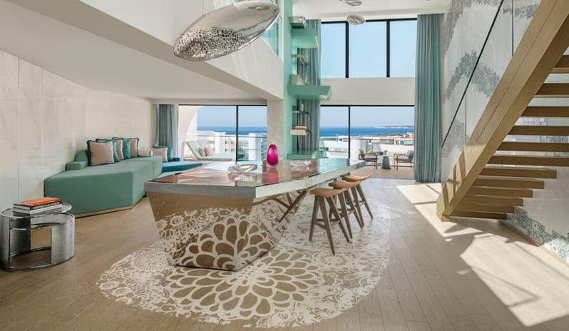 Penthouse II Suite, One Bedroom Suite with Pool  living area with high ceilings, a modern wooden staircase, and a large decorative dining island overlooking the ocean through floor-to-ceiling windows at W Algarve by Kenwood Travel
