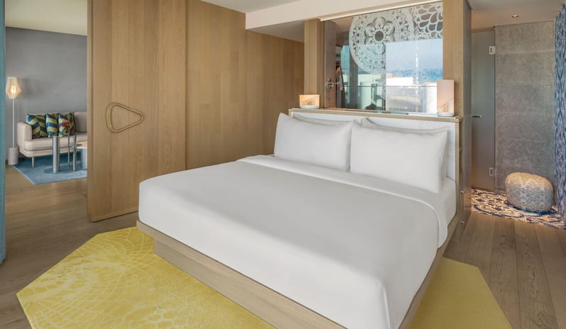 Premier Two-Bedroom Residence bedroom in the Premier 2-Bedroom Suite at W Algarve, featuring a white king bed, a vibrant yellow rug, and a large light-wood sliding door leading to a separate living area at W Algarve by Kenwood Travel