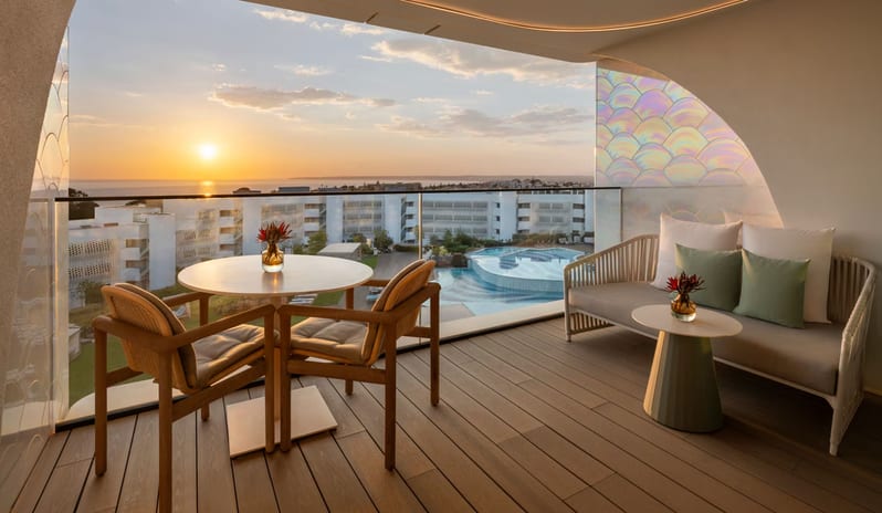 Premier Deluxe Room private terrace at sunset featuring modern outdoor lounge furniture, a dining set, and iridescent glass partitions, overlooking a resort pool and the ocean at W Algarve by Kenwood Travel