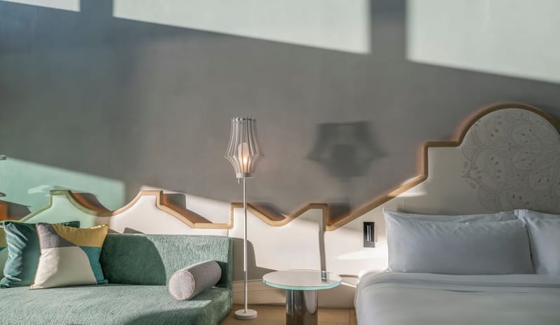 Premier Private Garden Room contemporary bedroom design showing a custom zig-zag backlit wall feature, a minimalist white floor lamp, and a teal sofa under natural window light at W Algarve by Kenwood Travel