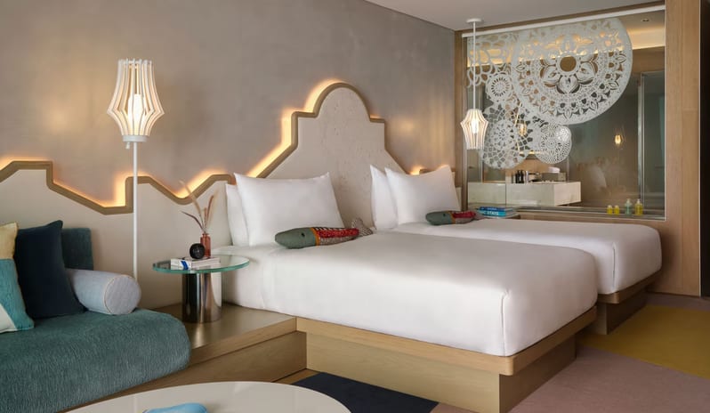 Superior Room two single beds with white linens, a decorative scalloped headboard with warm backlight, and a glass partition separating the bedroom from a sleek bathroom at W Algarve by Kenwood Travel