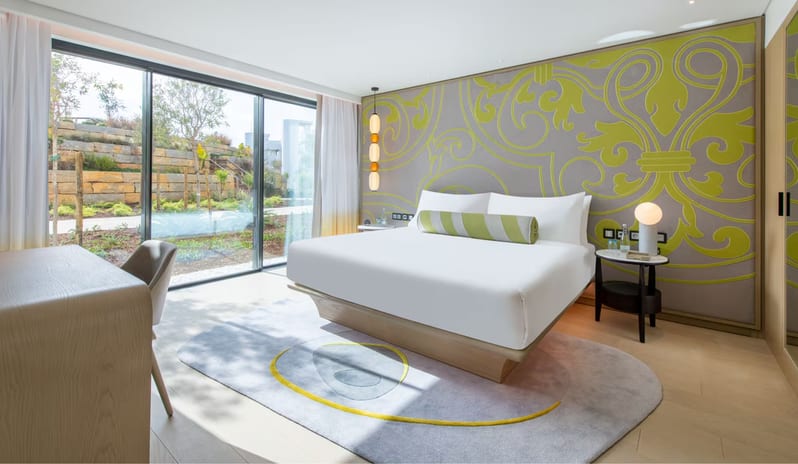 Premier One-Bedroom Residence bedroom featuring a lime green and grey damask accent wall, a floating platform bed with white linens, and floor-to-ceiling glass doors opening to a landscaped garden at W Algarve by Kenwood Travel
