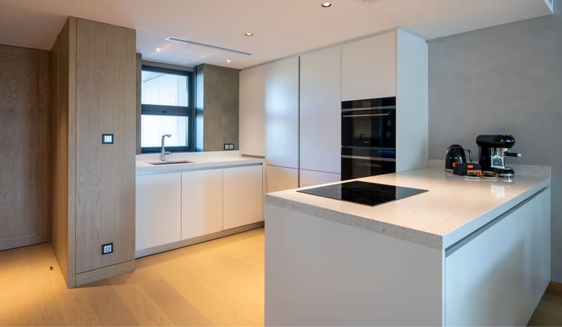 Supreme Two Bedroom Suite kitchen featuring white handleless cabinetry, a large kitchen island with a built-in black induction cooktop, and integrated double ovens at W Algarve by Kenwood Travel