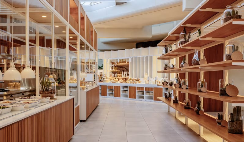 Malva Food Bazaar Restaurant interior featuring a large backlit stone relief wall mural, modern teal rope chairs, and elegantly set tables with wine glasses and gourmet plates at Paradisus Salinas Lanzarote by Kenwood Travel