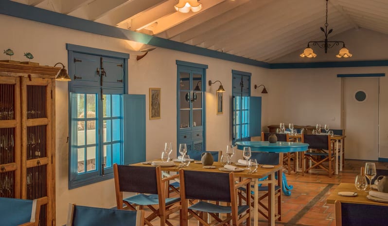 La Graciosa Restaurant with warm lighting, blue window shutters, wooden cabinets, and set dining tables with navy chairs at Paradisus Salinas Lanzarote by Kenwood Travel