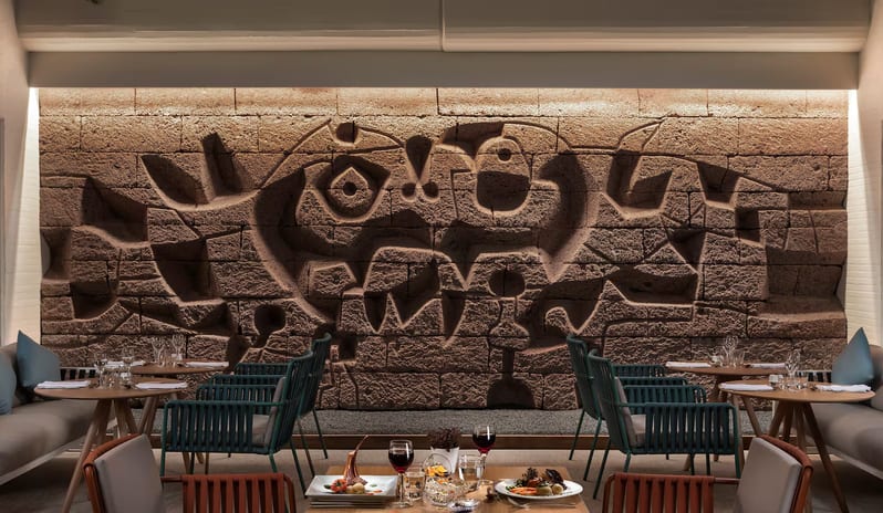 Malva Food Bazaar Restaurant interior featuring a large abstract stone relief wall mural in the style of Joan Miró, with elegant blue rope-weave chairs and soft lighting at Paradisus Salinas Lanzarote by Kenwood Travel