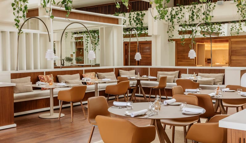 Samira restaurant interior featuring warm wood-paneled banquettes with cream cushions, tan leather armchairs, and round wooden tables set with white linens. at Paradisus Salinas Lanzarote by Kenwood Travel