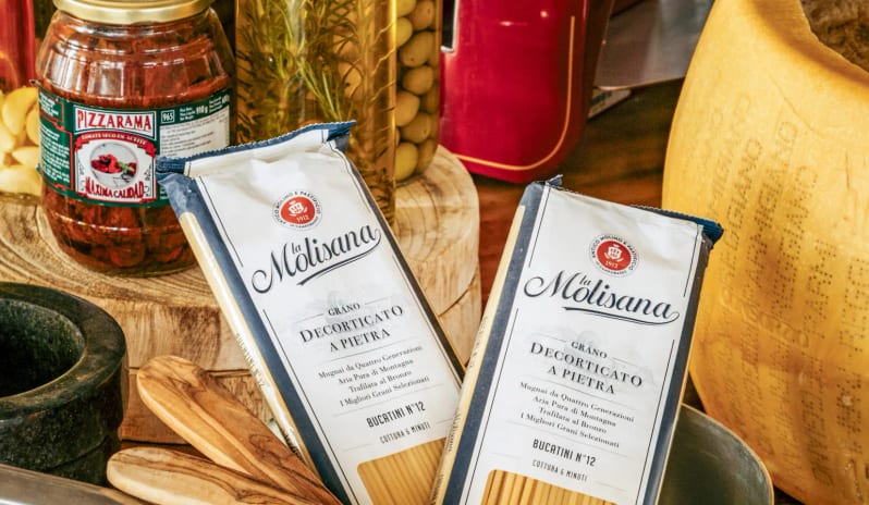 Cappella Italian Restaurant Packets of La Molisana pasta next to a giant cheese wheel, jars of sun-dried tomatoes, and a stone mortar and pestle at Paradisus Salinas Lanzarote by Kenwood Travel