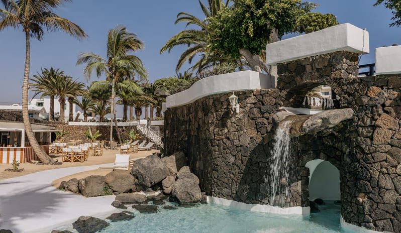 Beach Bar with white and orange striped counter, wooden director chairs, and palm trees against a volcanic stone wall at Paradisus Salinas Lanzarote by Kenwood Travel