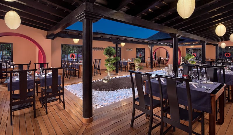 Wok-N-Zen Asian Fusion Restaurant Asian fusion dining terrace at night featuring traditional dark wood architecture, circular Moon gate entrances, and minimalist bonsai landscaping at a luxury resort at Sheraton Fuerteventura Beach, Golf & Spa Resort by Kenwood Travel