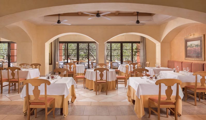 Los Arcos Buffet restaurant dining room featuring arched entryways, white-clothed tables with yellow linens, wooden chairs, and views of a lush garden through large windows at Sheraton Fuerteventura Beach, Golf & Spa Resort by Kenwood Travel
