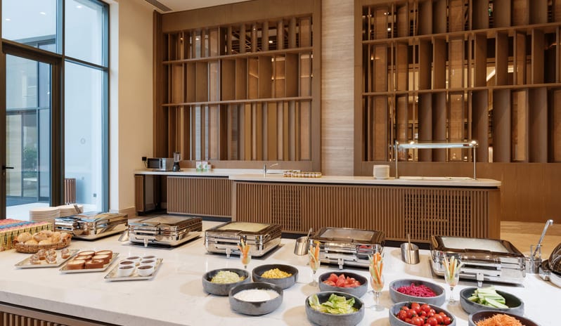 Pink Rabbit Kids Buffet featuring a selection of fresh salads in stone bowls, assorted breads, and hot catering dishes under a wooden slatted wall design at Anda Barut Collection by Kenwood Travel