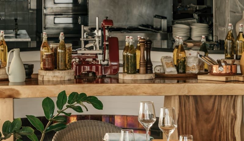 Cappella Italian Restaurant counter with olive oil bottles, a meat slicer, and Italian ingredients in front of an open kitchen at Paradisus Salinas Lanzarote by Kenwood Travel