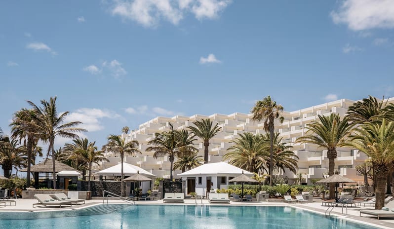 The Reserve Pool Bar beachfront resort featuring a tiered architectural design, outdoor swimming pool, and tropical palm trees on a sunny day at Paradisus Salinas Lanzarote by Kenwood Travel