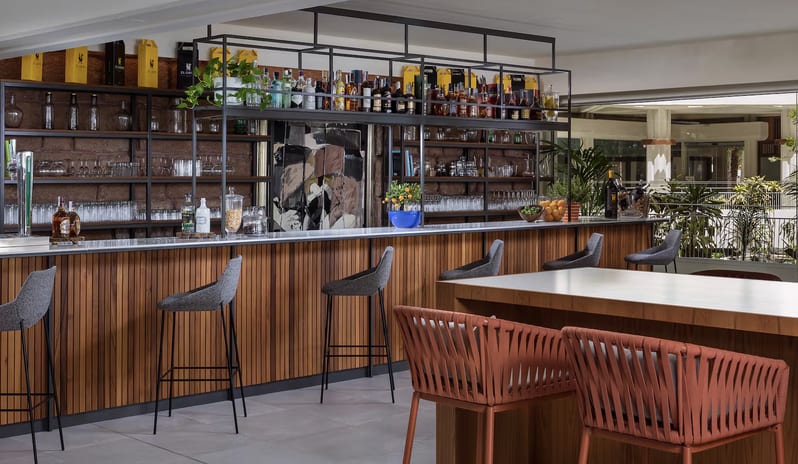 Ginger Lobby Bar with a wooden slat counter, grey bar stools, and terracotta-colored wicker chairs at Paradisus Salinas Lanzarote by Kenwood Travel