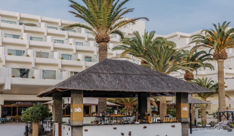 The Shack Poolside Terrace  beachfront resort courtyard surrounded by tall palm trees and a multi-story white hotel building with private balconies at Paradisus Salinas Lanzarote by Kenwood Travel