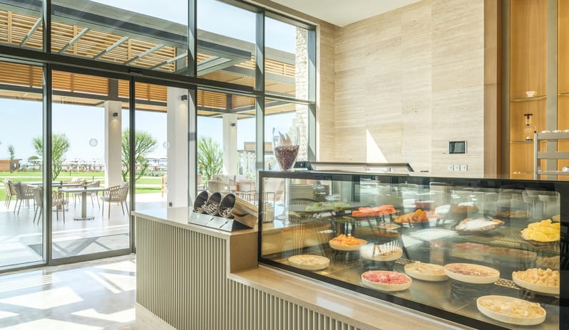Olivae Patisserie lounge with floor-to-ceiling windows, light wood herringbone floors, and various contemporary seating arrangements under a decorative beamed ceiling at Anda Barut Collection by Kenwood Trave