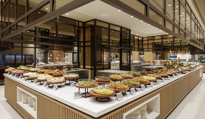 Zestful Bazaar Main Restaurant variety of gourmet appetizers and salads displayed on a modern white marble buffet counter with wooden accents and glass partitions in a bright restaurant at Anda Barut Collection by Kenwood Travel