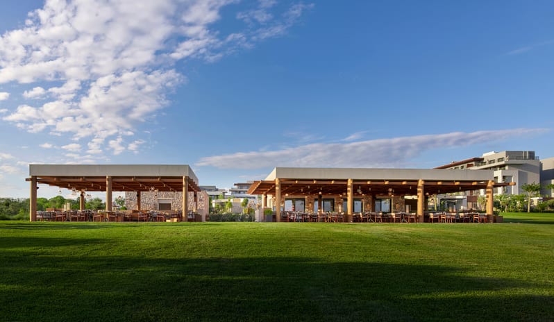 No Se Restaurant open-air dining pavilions with stone accents and wooden beams, situated on a sprawling, manicured green lawn at a luxury resort under a blue sky at Anda Barut Collection by Kenwood Travel