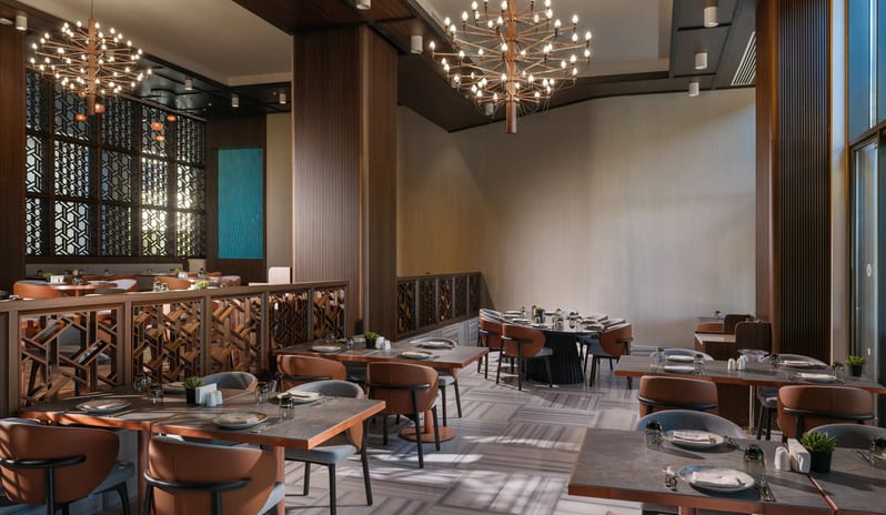 Kara Restaurant interior featuring modern starburst chandeliers, marble striped flooring, and contemporary seating with wood-paneled columns and decorative lattice dividers at Anda Barut Collection by Kenwood Travel