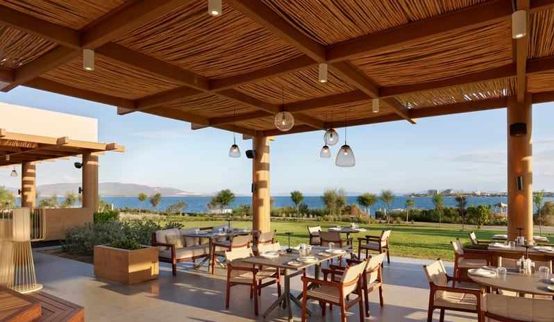 No Se Restaurant terrace featuring a rustic bamboo ceiling and wooden furniture, overlooking a green lawn and the blue sea at a luxury resort at Anda Barut Collection by Kenwood Travel