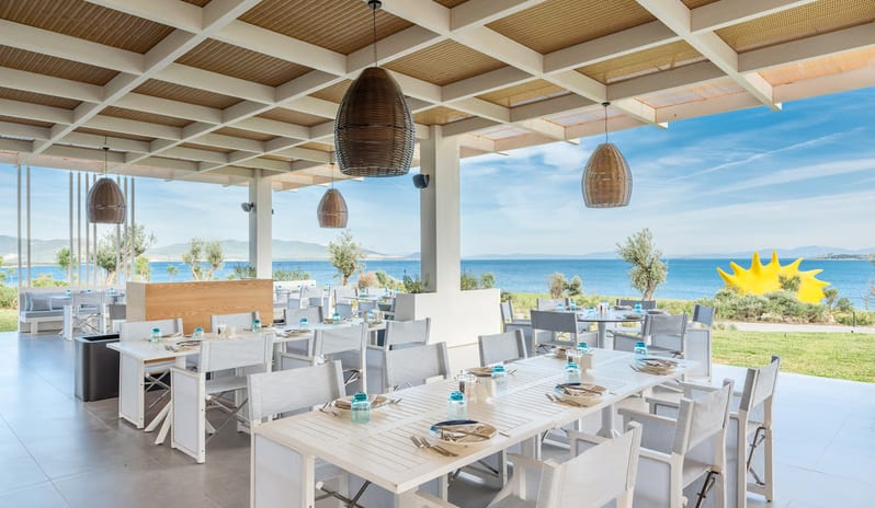 Fish Camp Restaurant outdoor restaurant terrace with white wooden dining tables, woven basket pendant lights, and a coffered ceiling offering a panoramic view of the blue ocean and coastline at Anda Barut Collection by Kenwood Travel