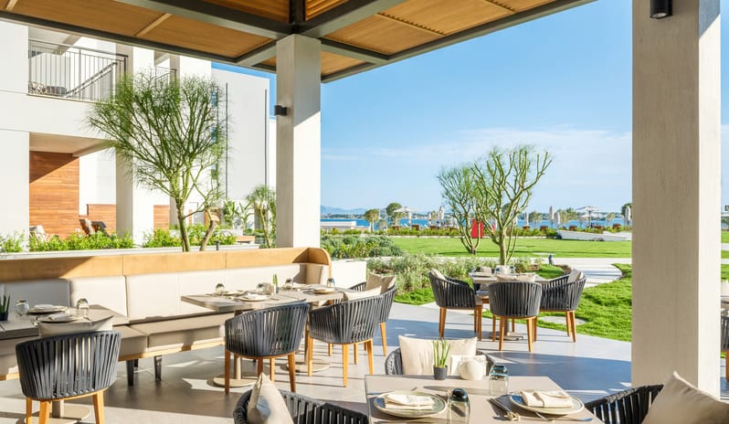 Tiger Restaurant outdoor dining area at a luxury hotel with stylish patio furniture and a scenic view of coastal greenery under a clear blue sky at Anda Barut Collection by Kenwood Travel