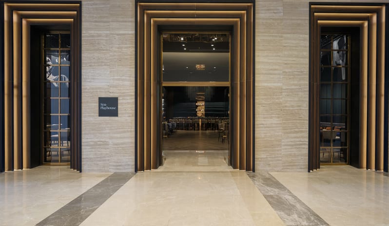 Soa Playhouse three backlit tiered archways, travertine stone walls, and polished marble flooring leading to a luxury bar lounge at Anda Barut Collection by Kenwood Travel