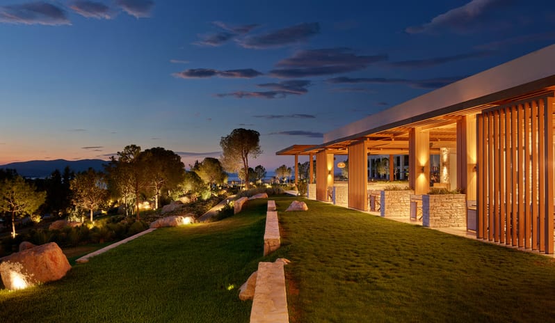 Mansion Restaurant International Kitchen evening view of a modern Mediterranean resort with illuminated stone pathways, terraced green lawns, and warm architectural lighting under a sunset sky at Anda Barut Collection by Kenwood Travel