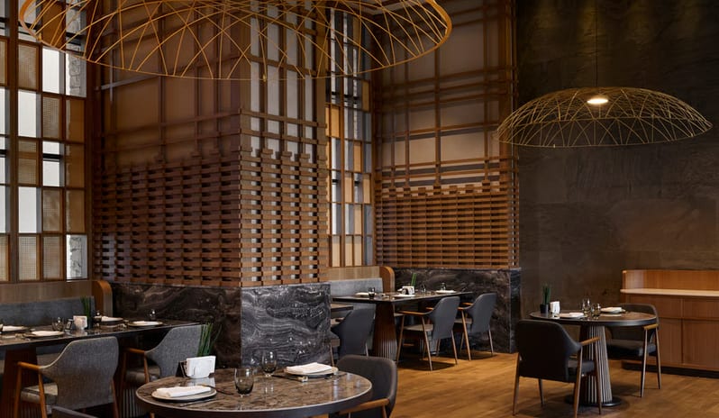 Tiger Restaurant dining space showcasing a blend of natural textures including dark marble wall cladding, light oak flooring, and architectural wooden screen partitions under warm ambient lighting